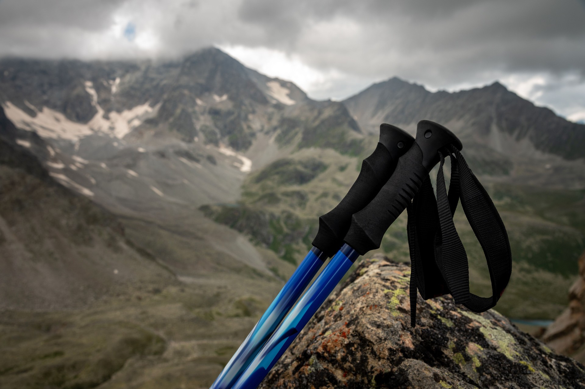 trekking poles close-up, lie on a stone overgrown with grass, in summer, against the backdrop of snow-capped rocky mountains